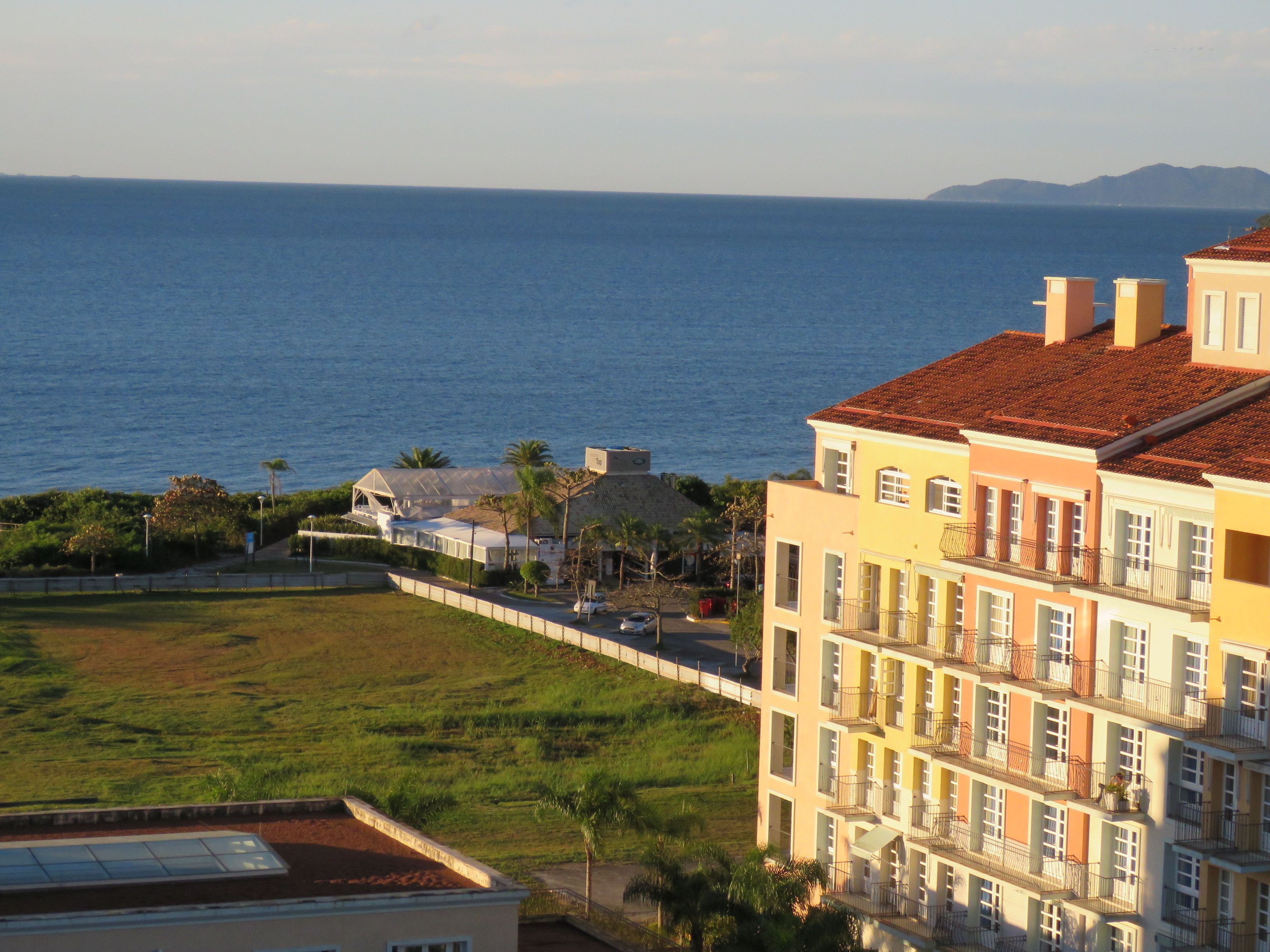 Un bâtiment situé sur la côte, doté de nombreux balcons, d’une pelouse à l’avant et offrant une vue sur la mer.