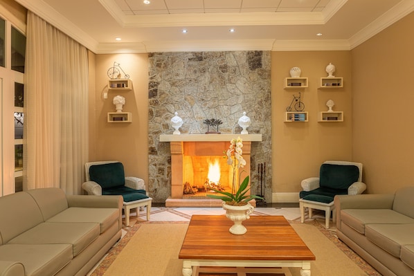 A cozy living room with a stone fireplace, two armchairs, a wooden coffee table, and a potted plant. - IL Campanario Villaggio Resort - OFICIAL (Florianópolis)