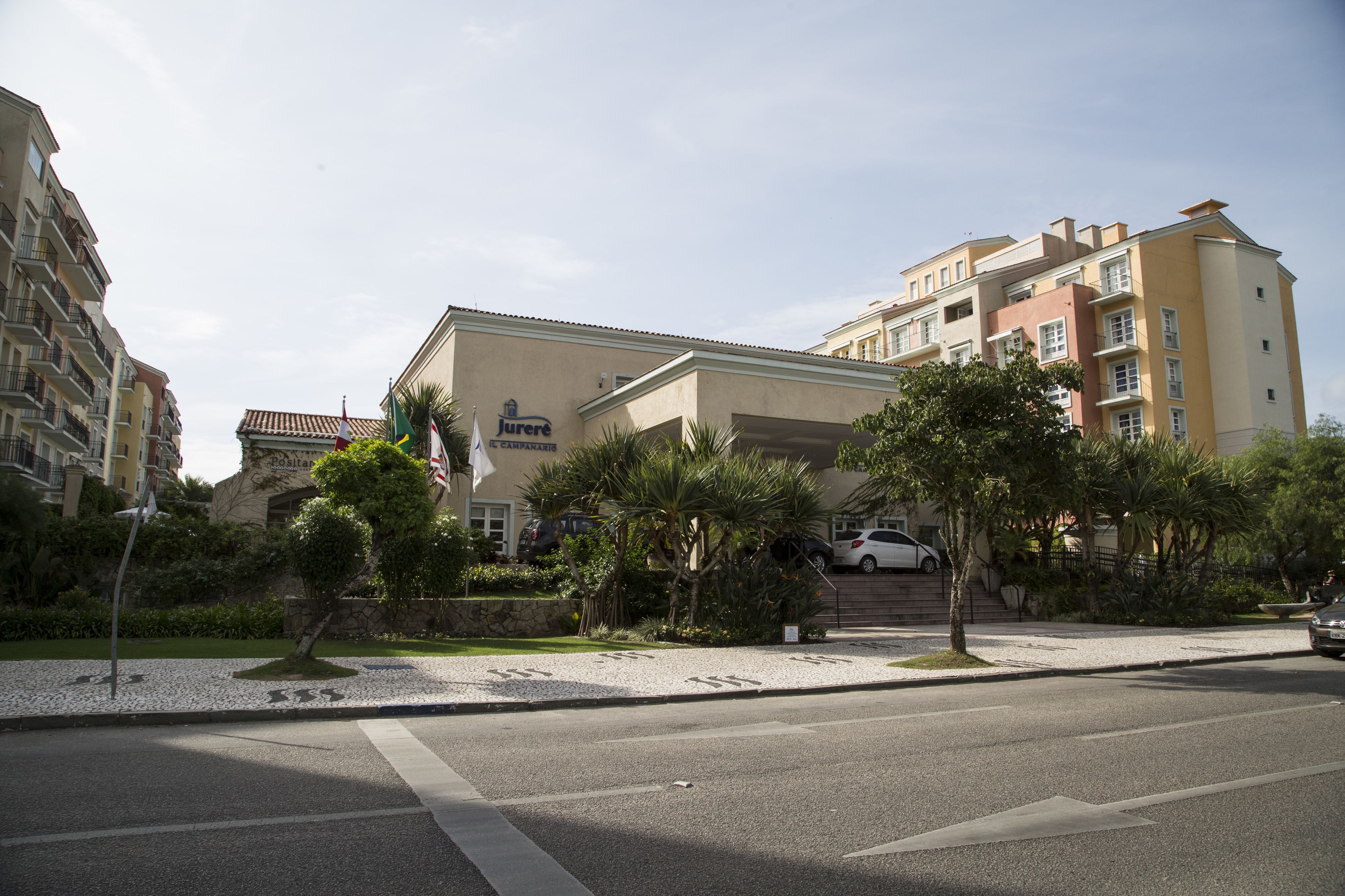 Un hotel de varios pisos con fachada color crema, un acceso cubierto y un estacionamiento con automóviles.