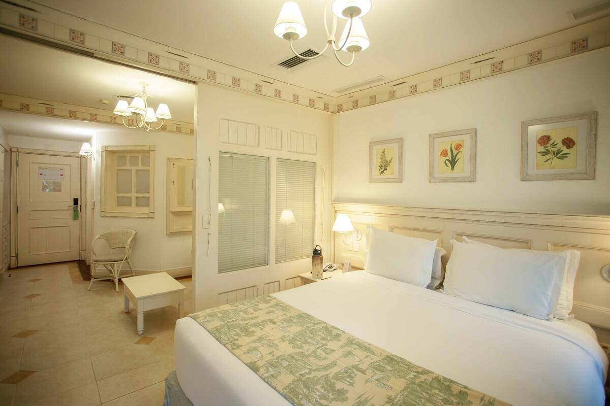 A hotel room with a bed, bedside lamps, a chair, a small table, and a door leading to a bathroom.