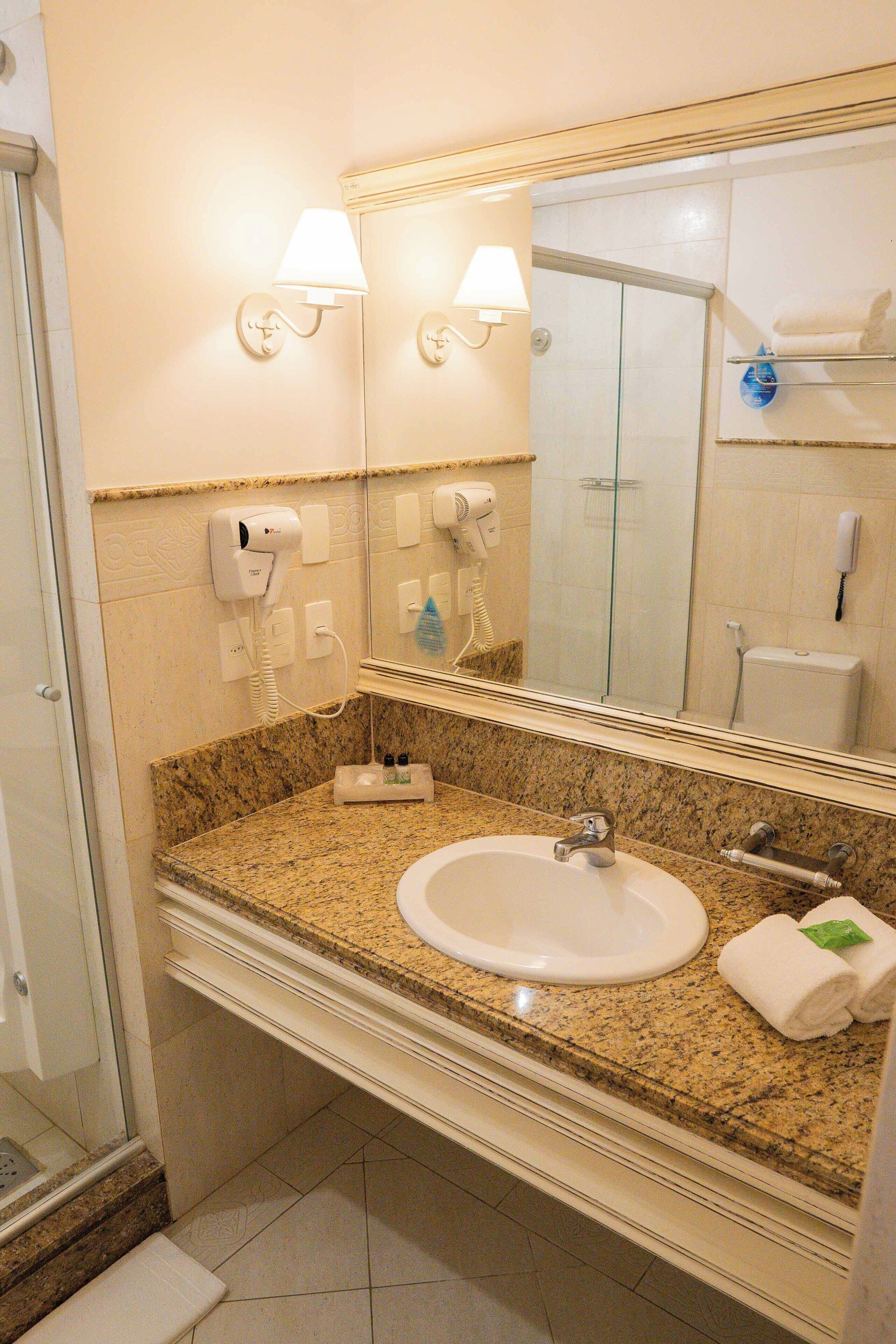 A bathroom with a granite countertop, a sink, a mirror, a towel rack, and a glass shower enclosure.