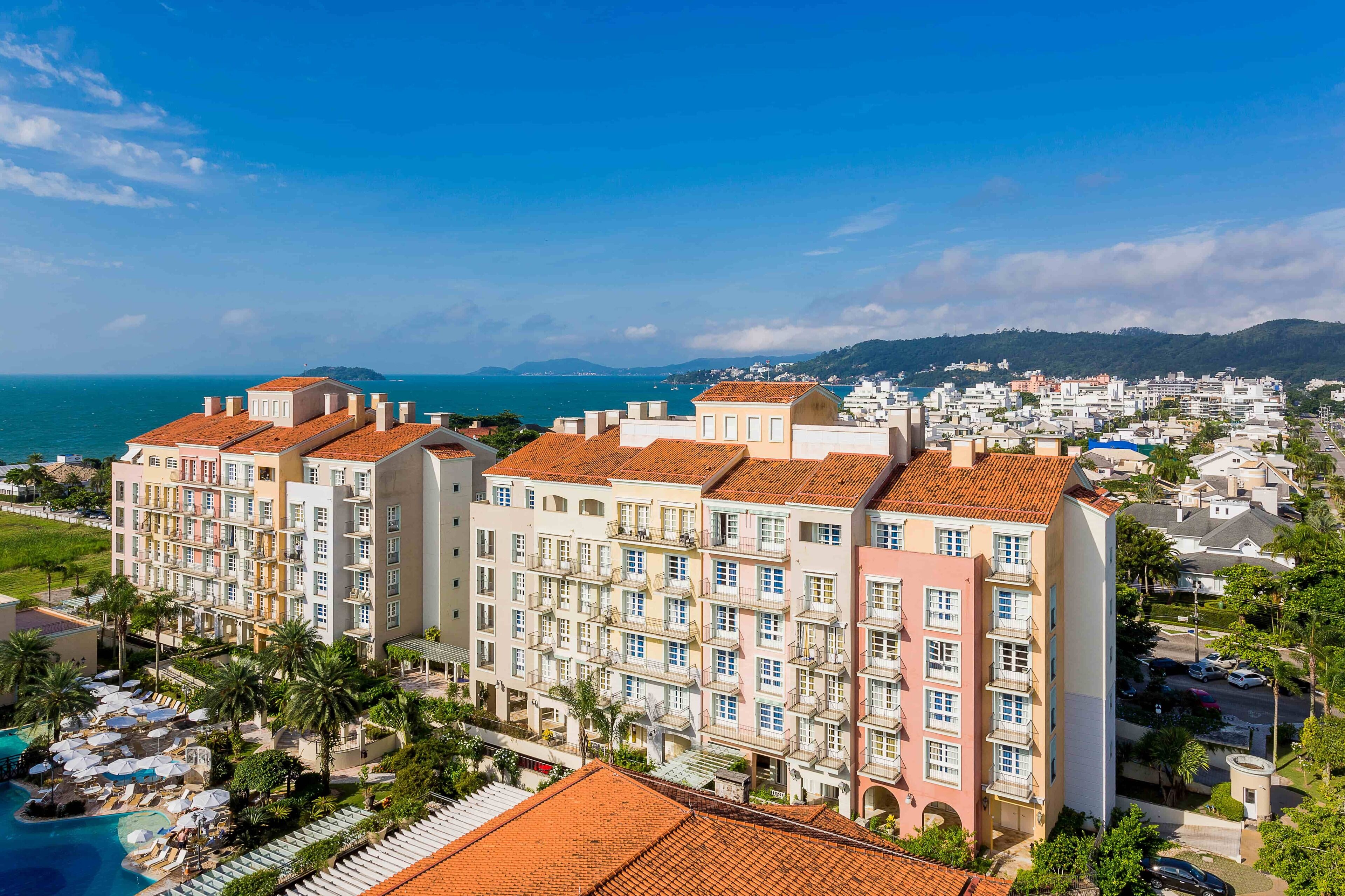 Un hotel de varios pisos con piscina en la azotea y vista al mar.
