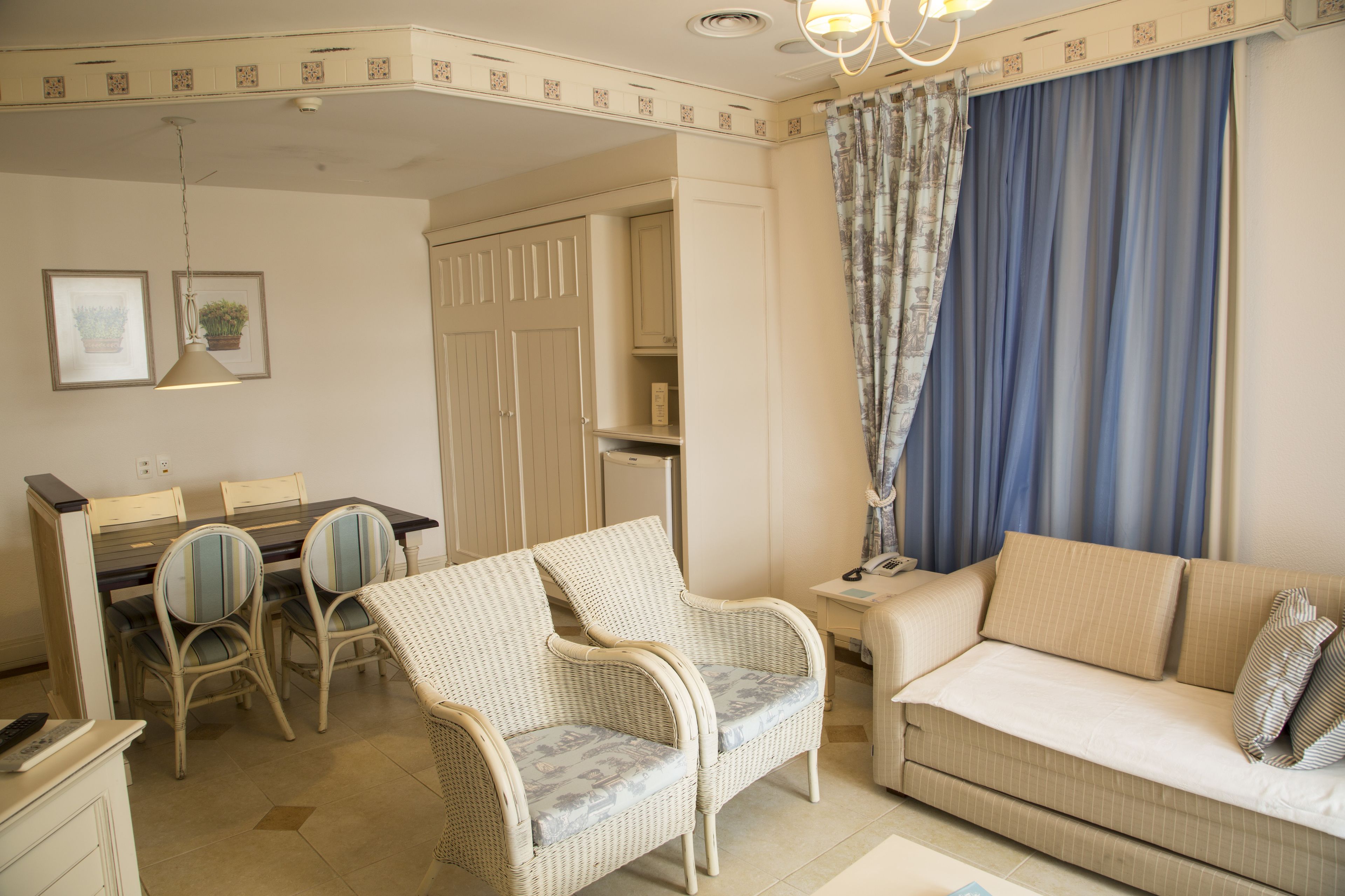 Un salon comprenant un canapé, deux fauteuils, une table à manger avec des chaises, une petite table d’appoint et une armoire.