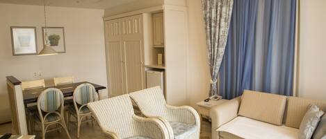 Un salon comprenant un canapé, deux fauteuils, une table à manger avec des chaises, une petite table d’appoint et une armoire.