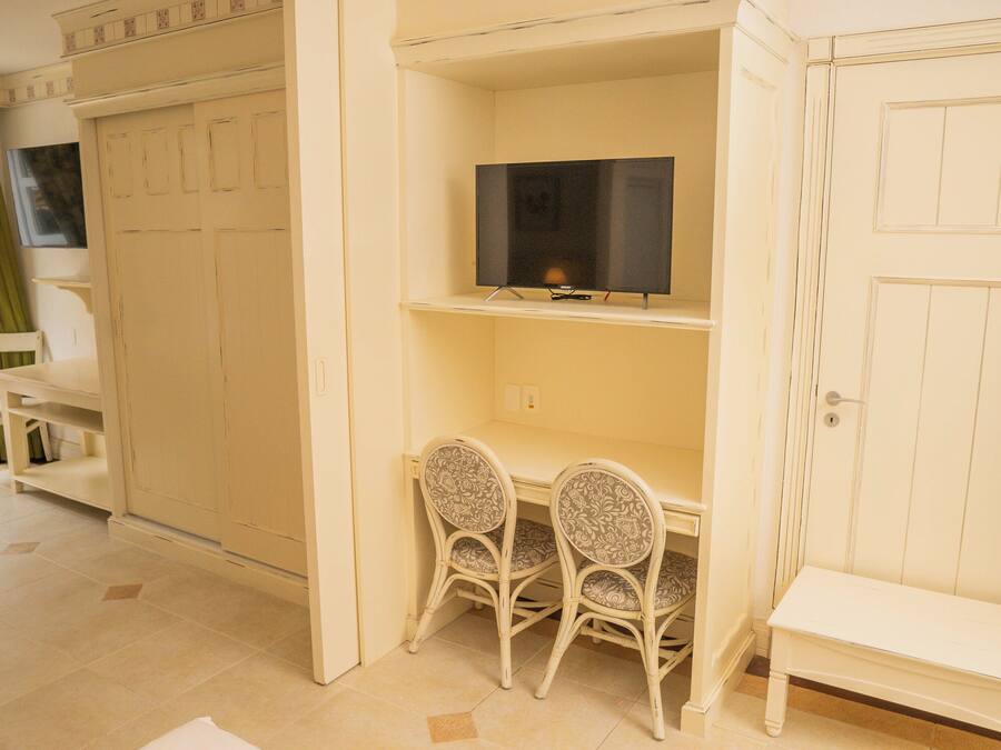 Una habitación con escritorio, dos sillas, televisor en un estante y armario.