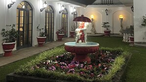 Un patio central con una fuente, rodeado de plantas en macetas y un sendero bien iluminado.