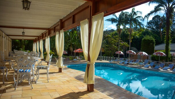 Un área junto a la piscina con sillones de descanso y sombrillas, un espacio cubierto con mesas y sillas, y vista despejada a la piscina.
