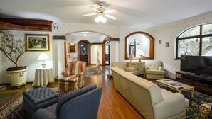 A spacious living room with a high ceiling fan, a television, and a large window providing natural light. - Biazi Paradise Hotel (Serra Negra)