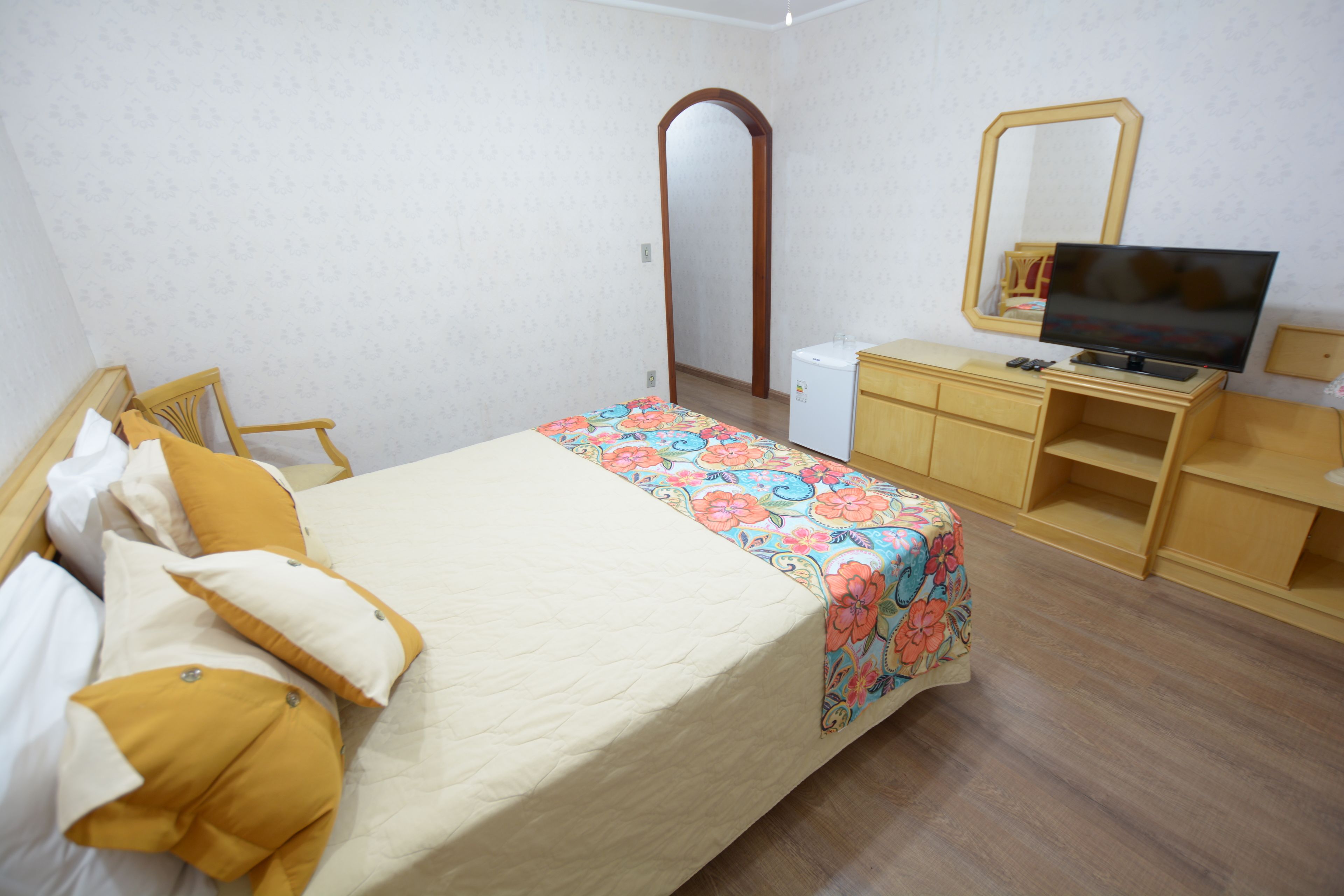 A bedroom with a bed, a dresser, a television, and a mirror.