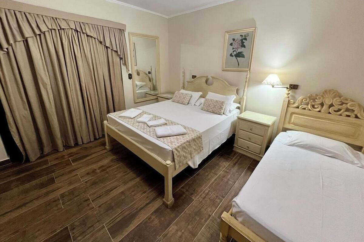 Habitación de hotel con una cama grande, una mesita de noche, un espejo y un cuadro en la pared.