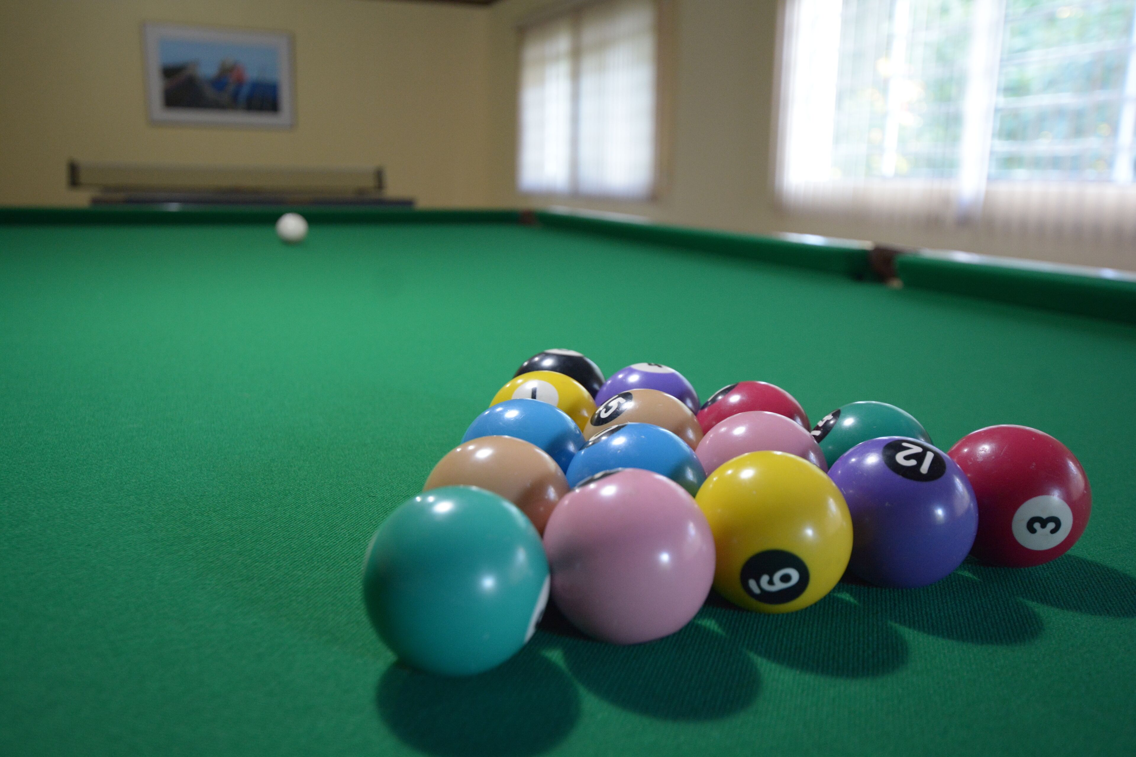 A pool table with colorful balls and a white ball in the distance.