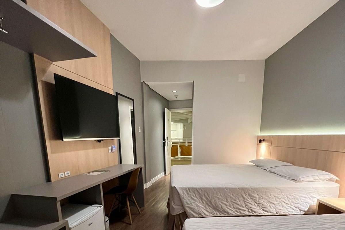 A hotel room with a flat-screen TV, a desk, two beds, and a ceiling light.
