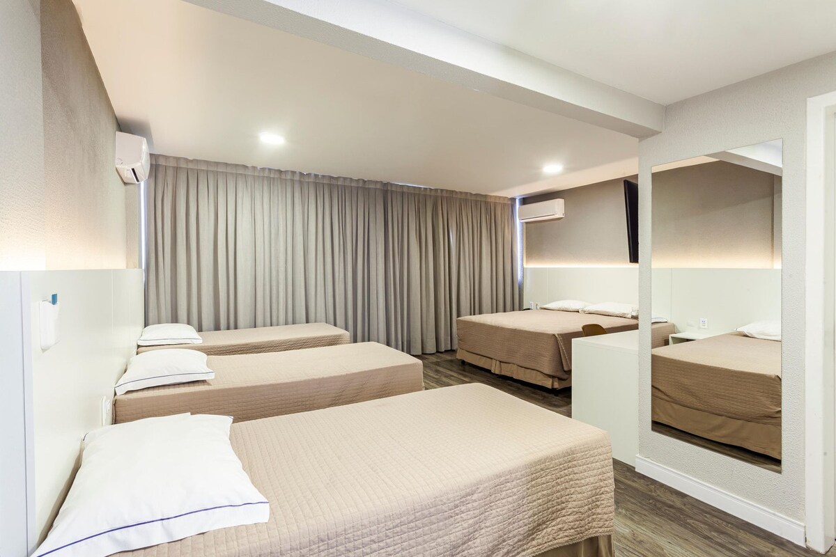 A hotel room with three single beds, a large mirror, and a ceiling-mounted air conditioning unit.