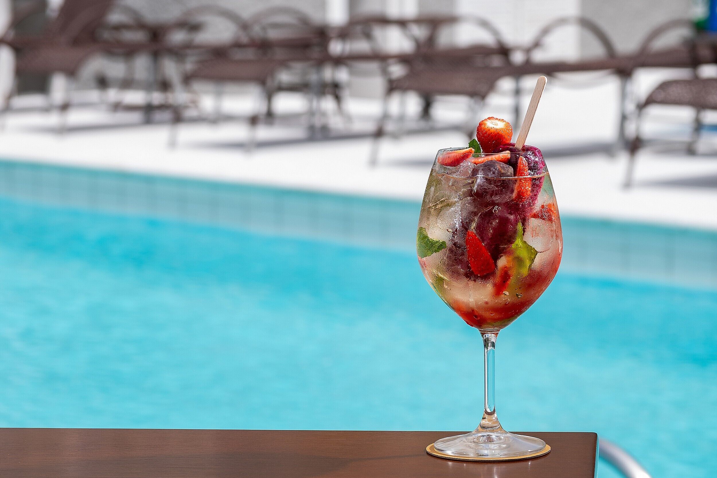 Um copo de cocktail com fruta e gelo sobre uma mesa perto de uma piscina.
