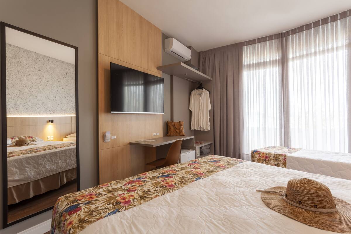 A hotel room with a bed, a desk, a TV, a mirror, and a window with curtains.