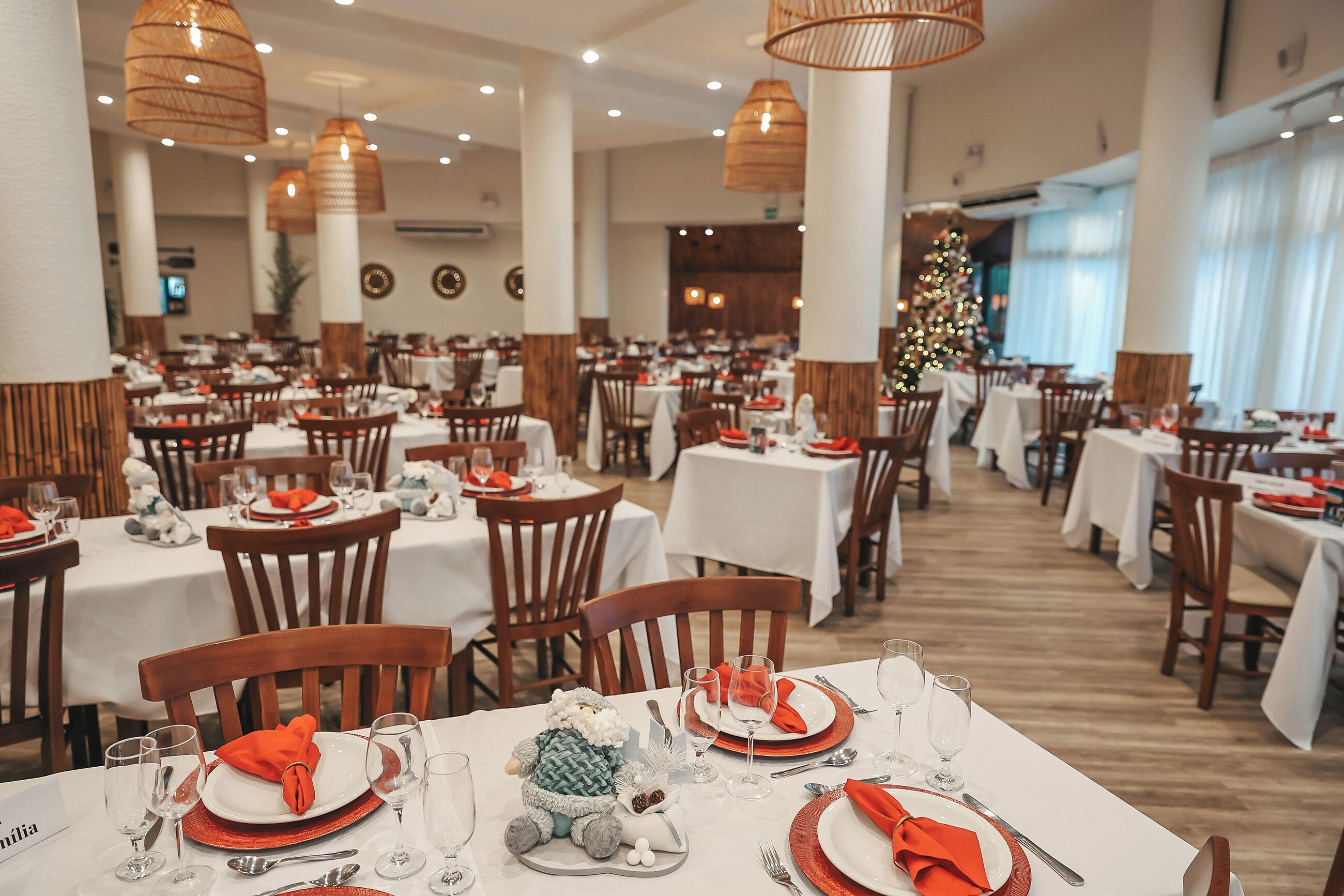 Un restaurante con varias mesas dispuestas para comer, con manteles blancos, sillas de madera y servilletas rojas.