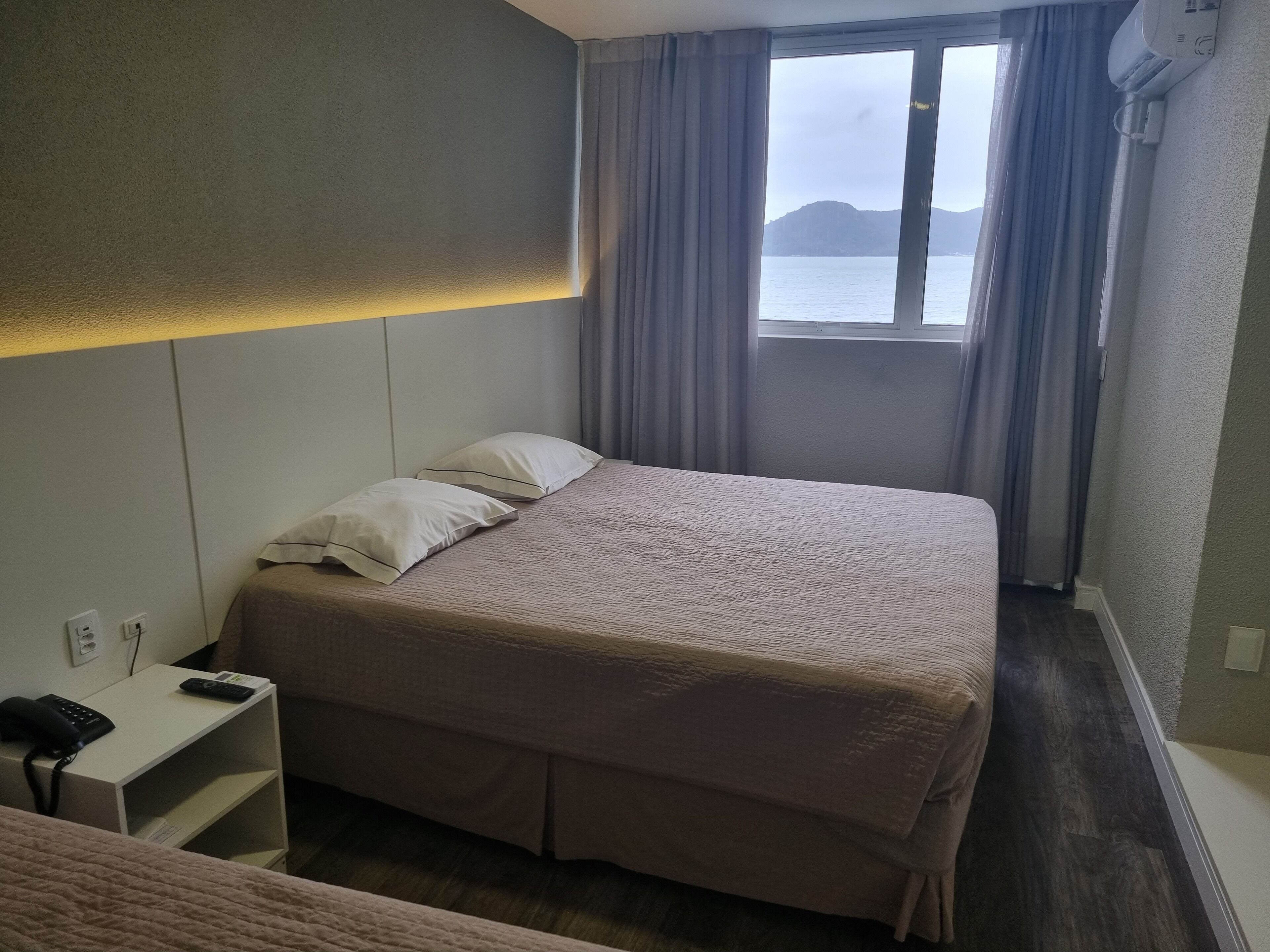 A hotel room with a bed, a bedside table with a phone, and a window with curtains.