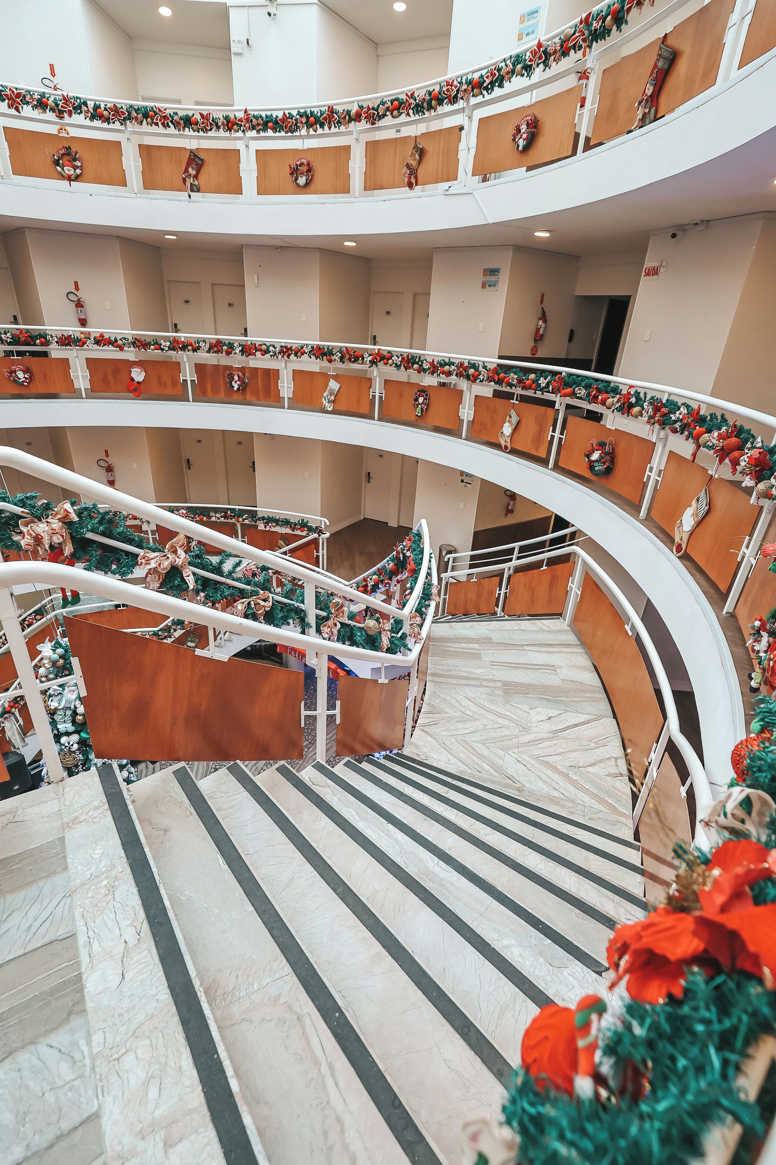 Ein mehrgeschossiges Innenraum mit einer zentralen Treppe, umgeben von Geländern mit festlicher Girlande und Weihnachtskranz.