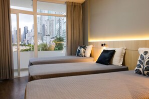 A hotel room with two beds, a large window with curtains, and a city view. - Marambaia Hotel & Convenções (Balneário Camboriú)