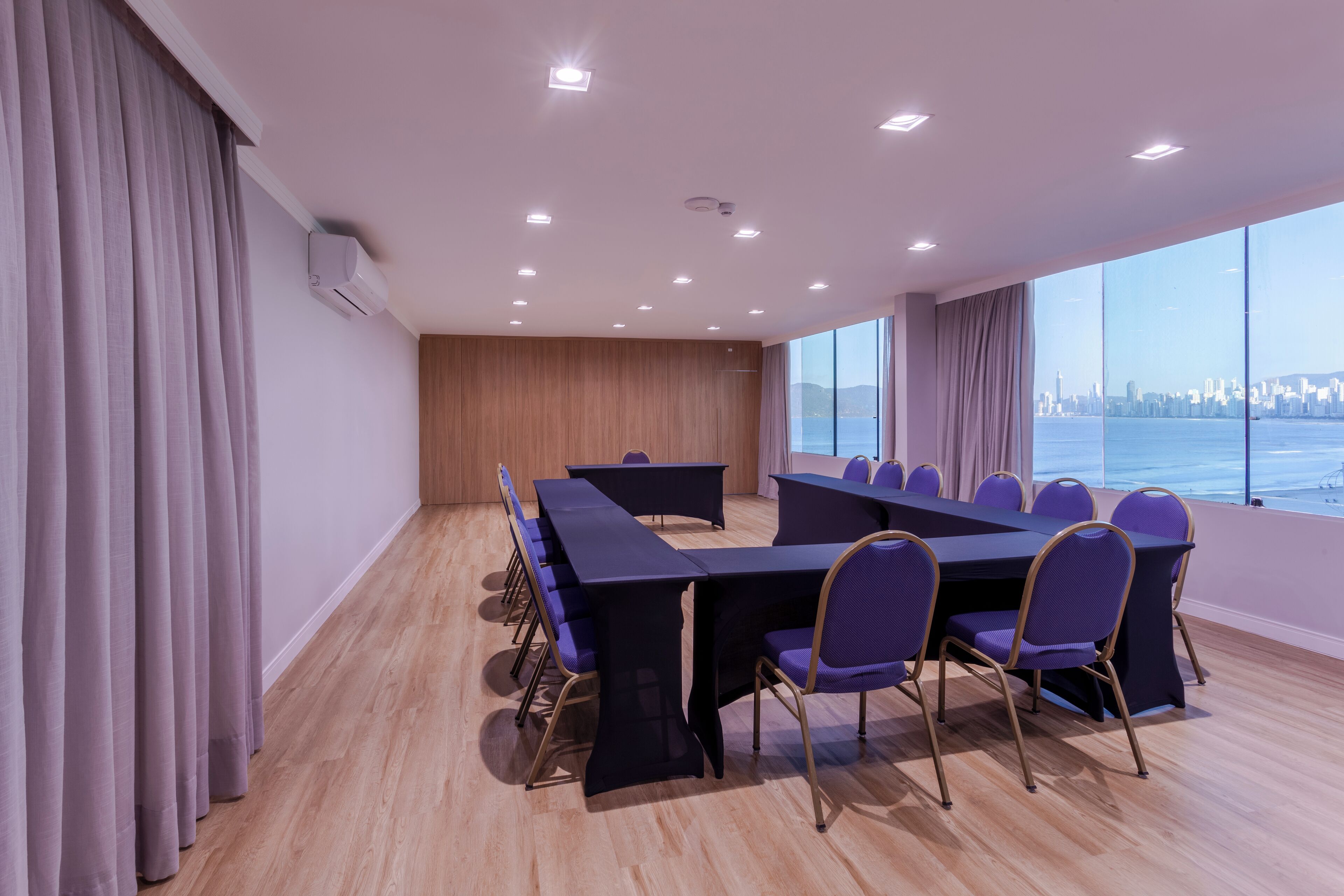 Una sala de conferencias con una larga mesa y sillas, ventanas amplias con vistas a la ciudad y suelo de madera.