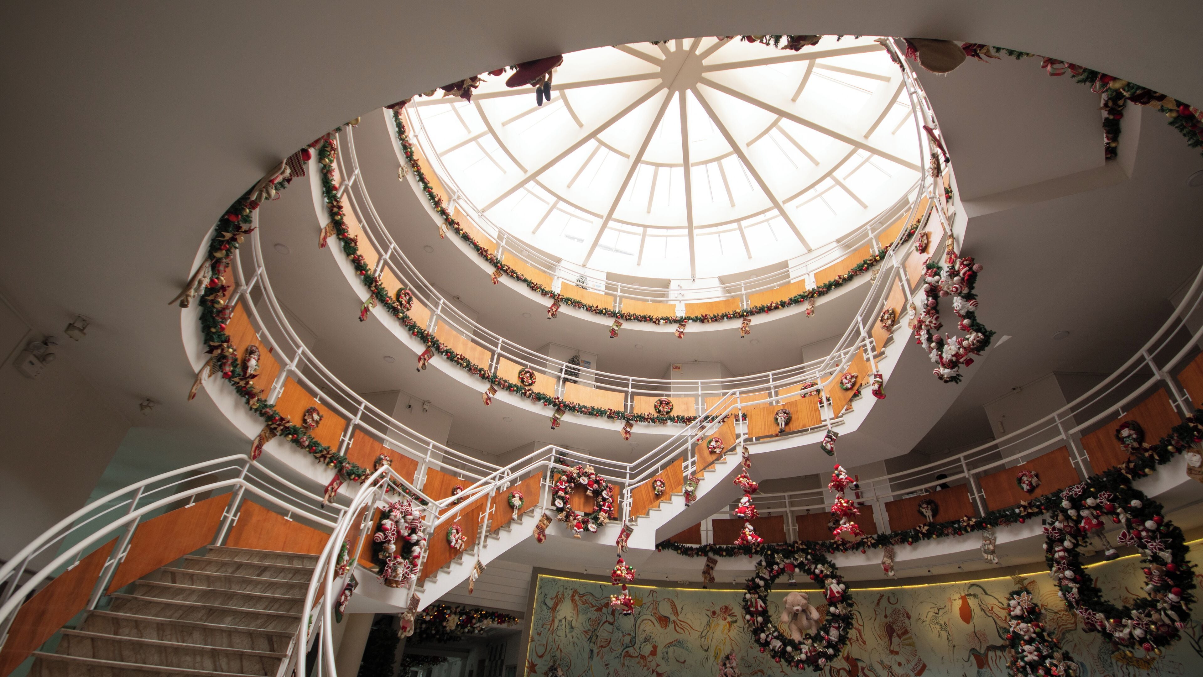 A multi-level atrium with a central glass dome, decorated with Christmas wreaths and garlands.