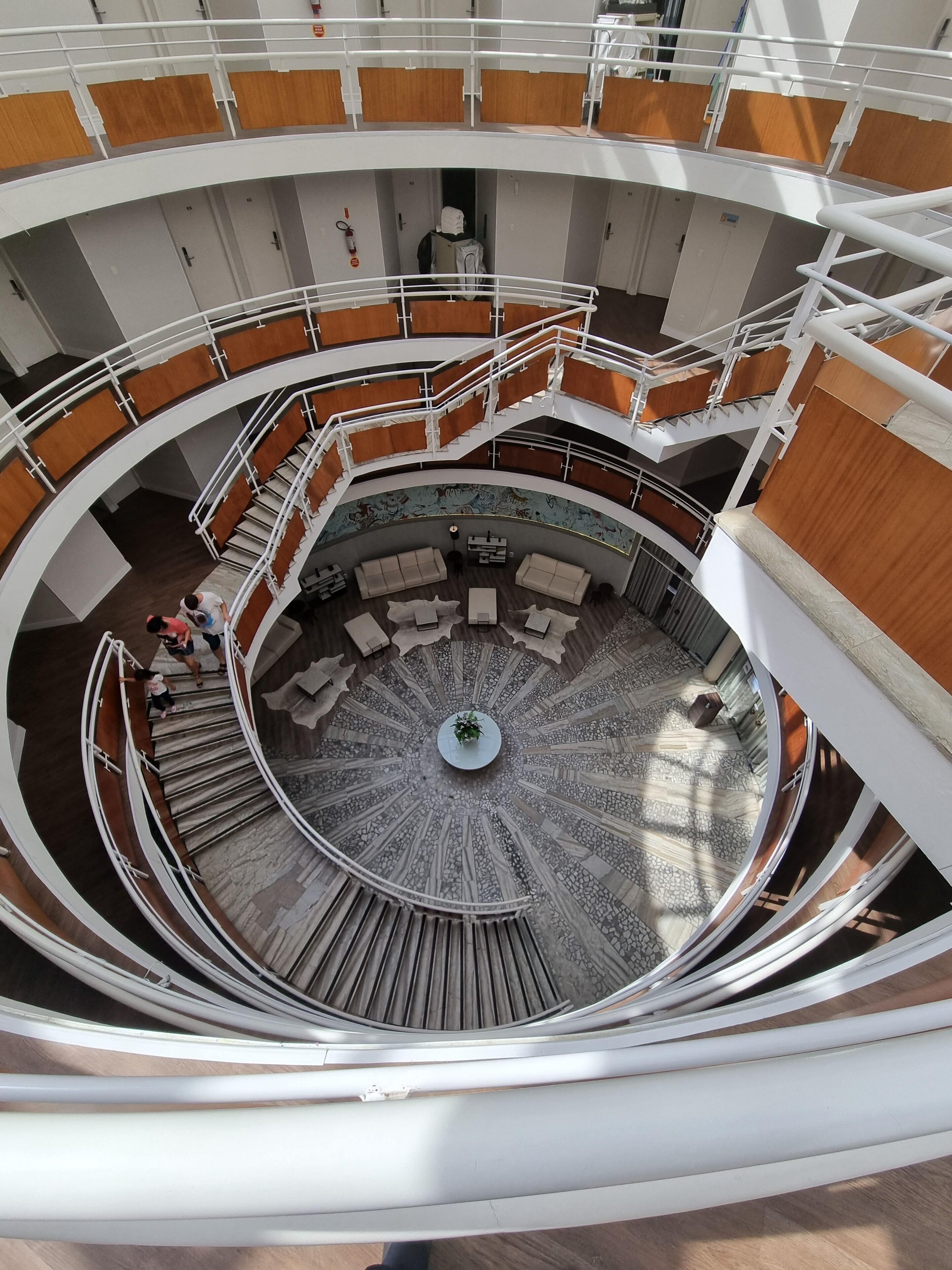 A multi-level atrium with a central circular seating area, multiple staircases, and wooden paneling.