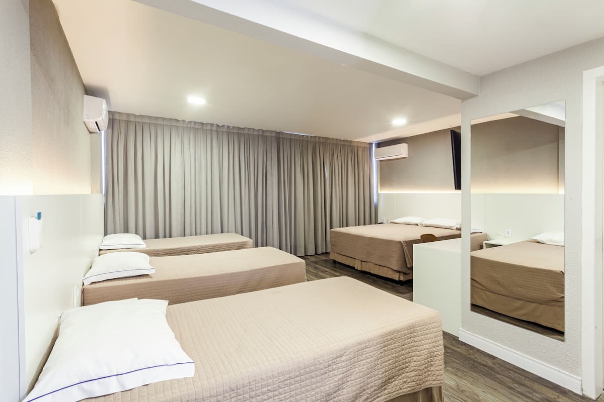 A hotel room with three single beds, a large mirror, a ceiling-mounted air conditioner, and a window with curtains.