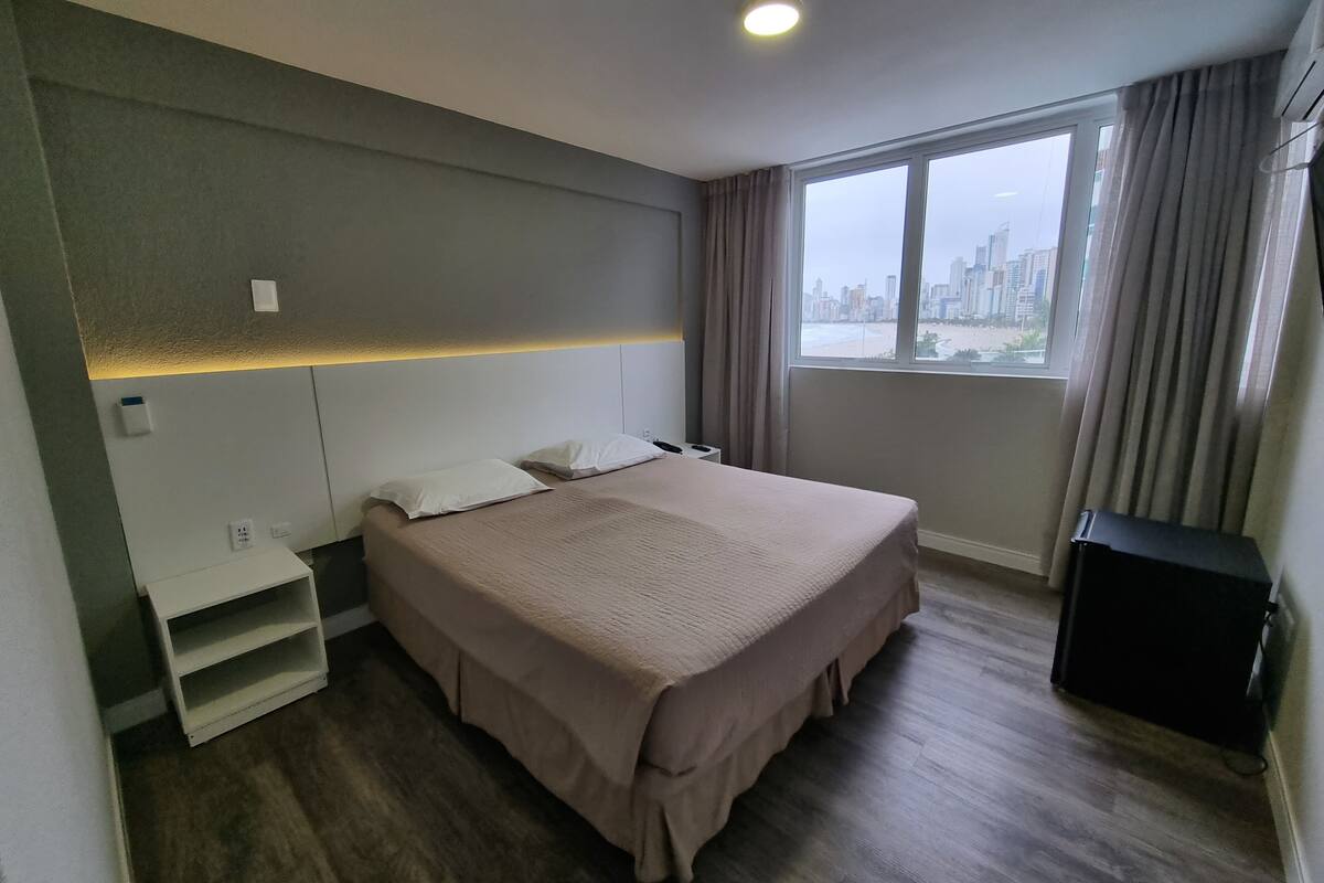 A hotel room with a large bed, a small bedside table, a wardrobe, and a window with a city view.