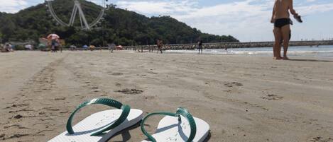 A pair of flip-flops on a sandy beach with a Ferris wheel and a person in the background.