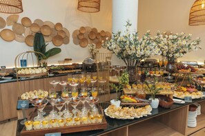 A buffet with various food items and drinks, including desserts and fruits, arranged on a counter. - Marambaia Hotel & Convenções (Balneário Camboriú)
