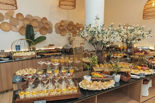 Un bufé con diversos alimentos y bebidas, incluyendo postres y frutas, dispuesto en una barra.