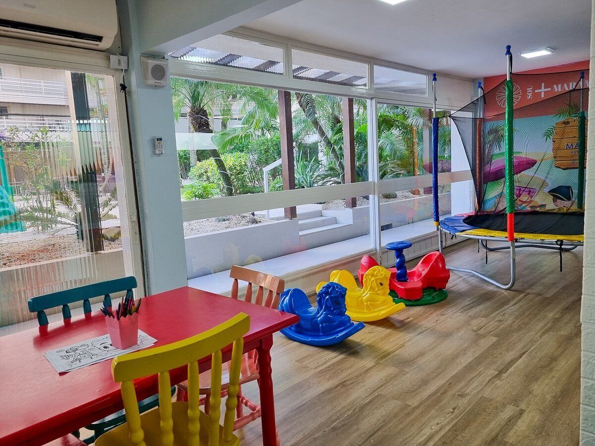 A children's play area with a red table, yellow and blue rocking horses, and a trampoline.