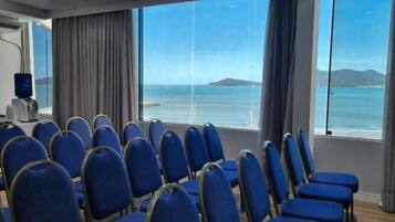 A conference room with rows of blue chairs facing a large window overlooking a body of water and distant land.