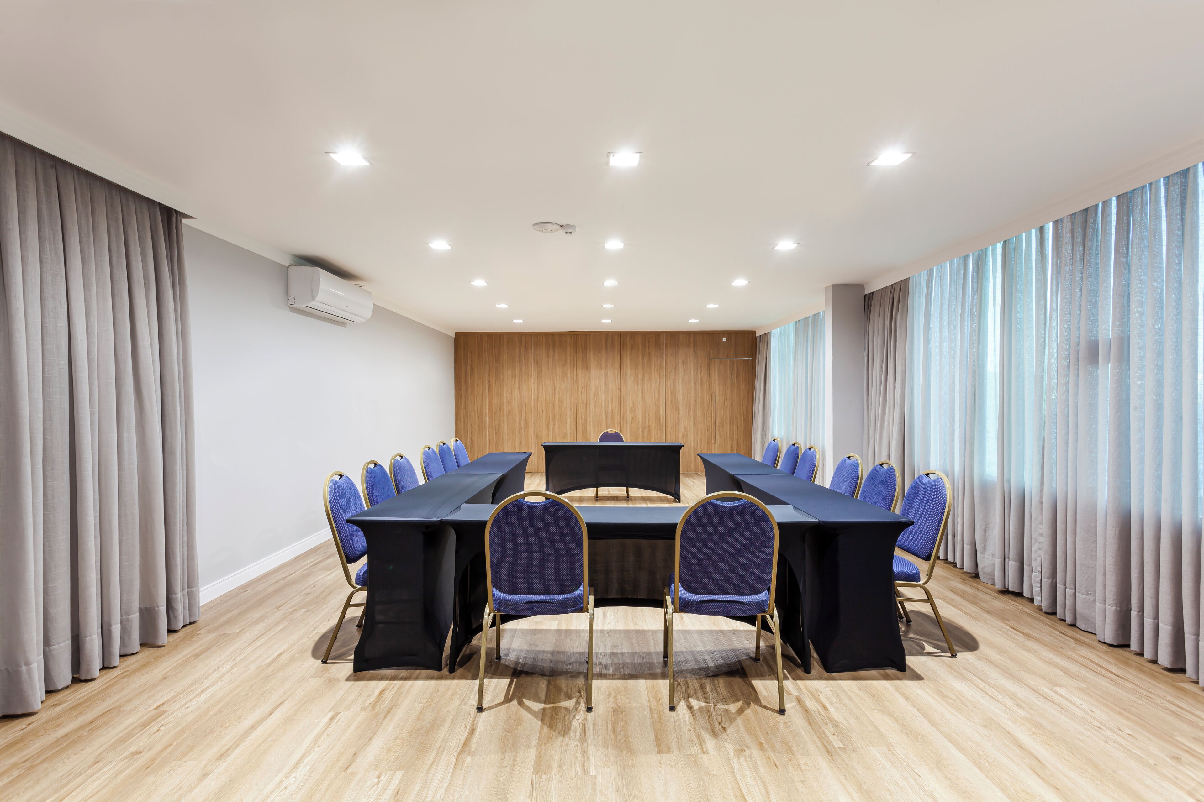A conference room with a long table, blue chairs, and a wooden panel wall.