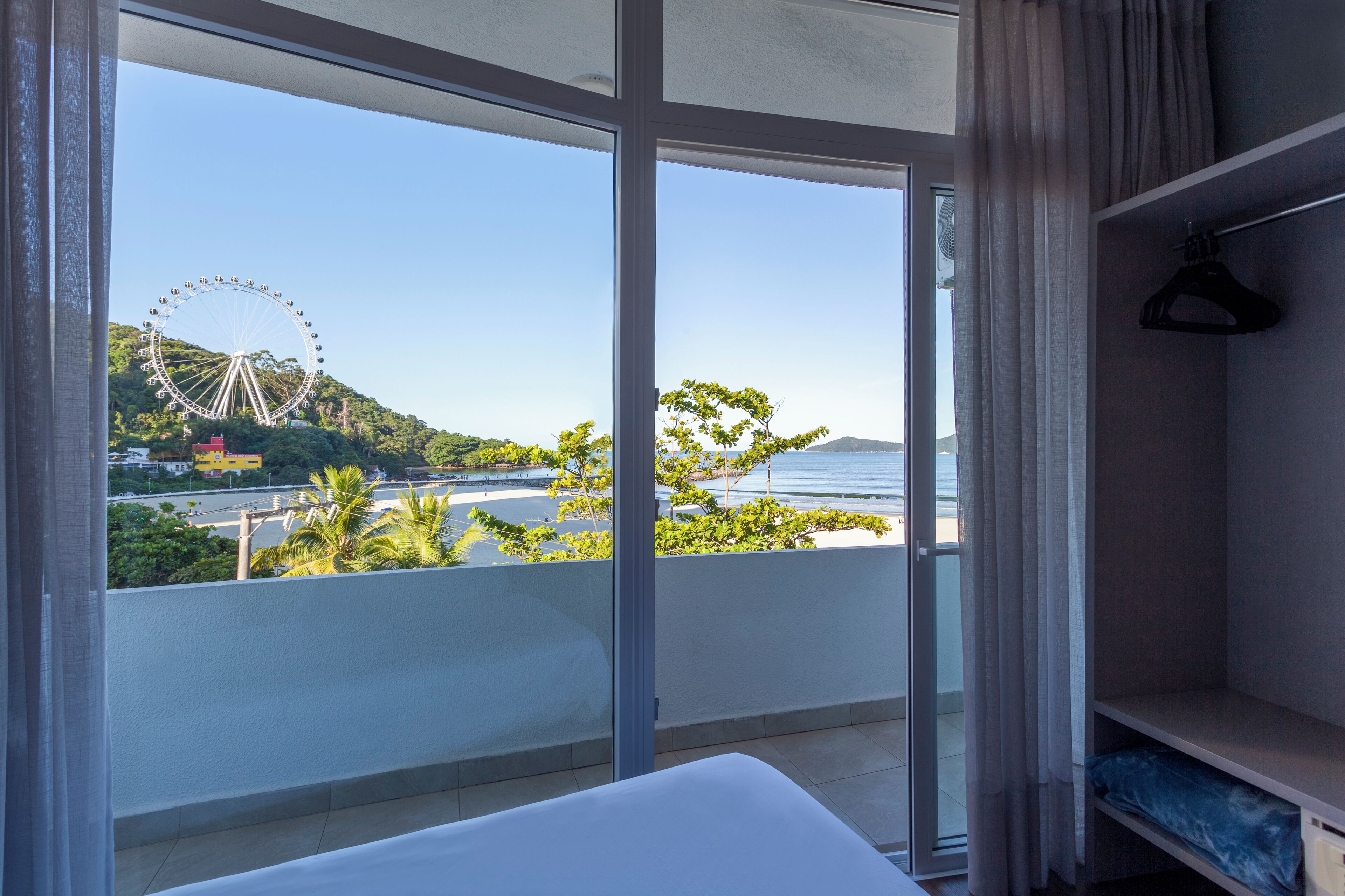 A hotel room with a large window offering a view of a Ferris wheel and greenery.