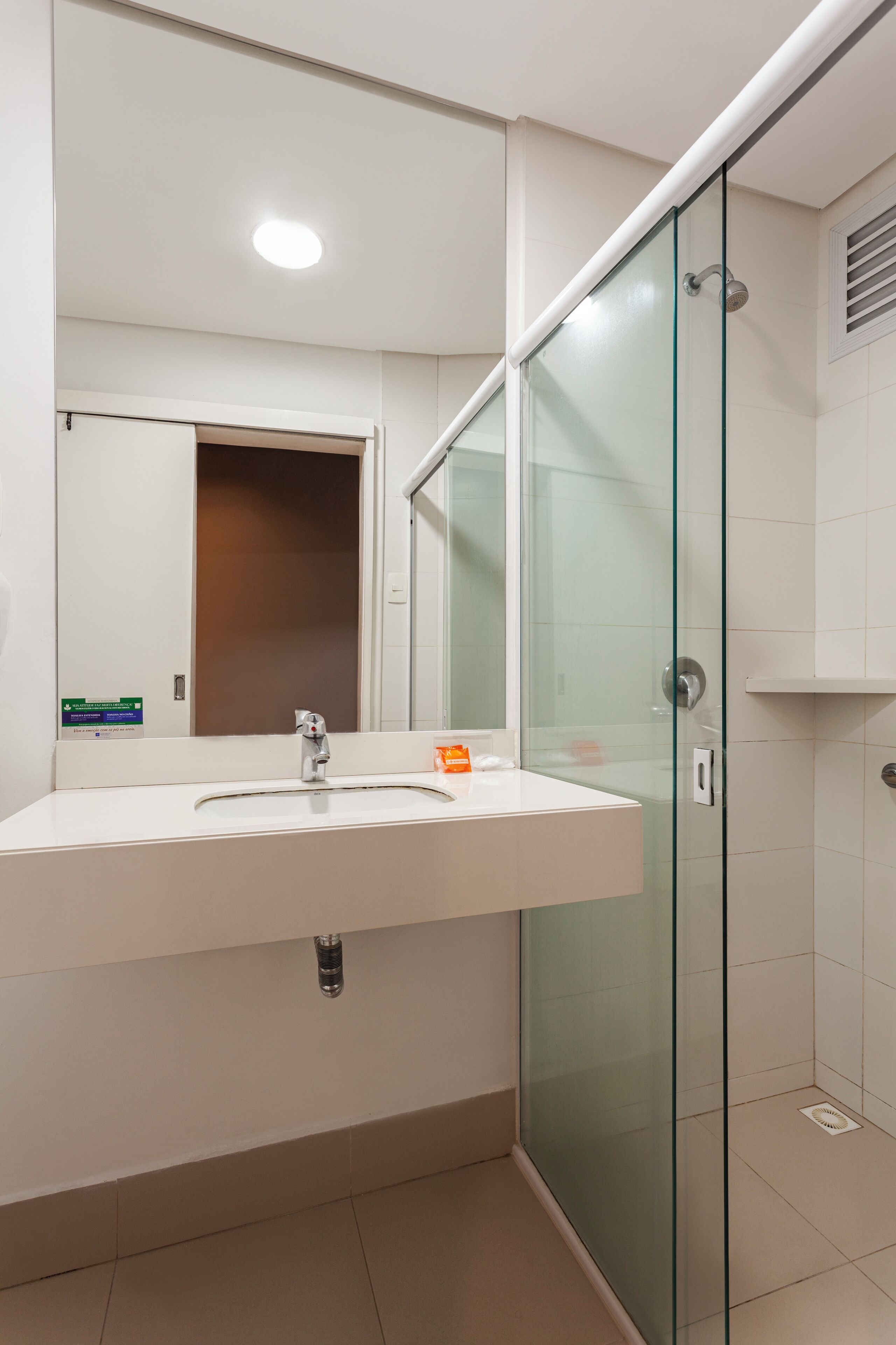 Un baño moderno con ducha de vidrio, lavamanos blanco y espejo arriba.