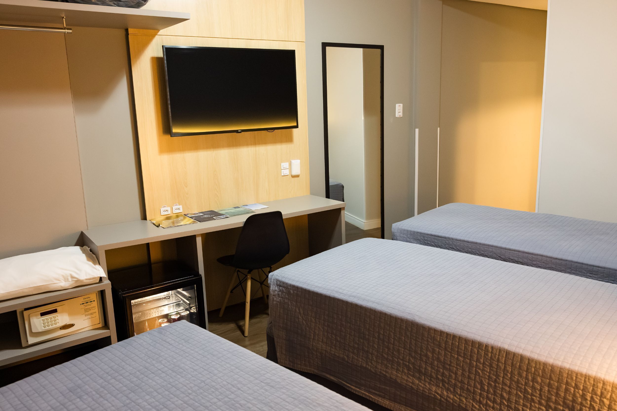 A hotel room with two beds, a desk with a chair, a television, and a refrigerator.