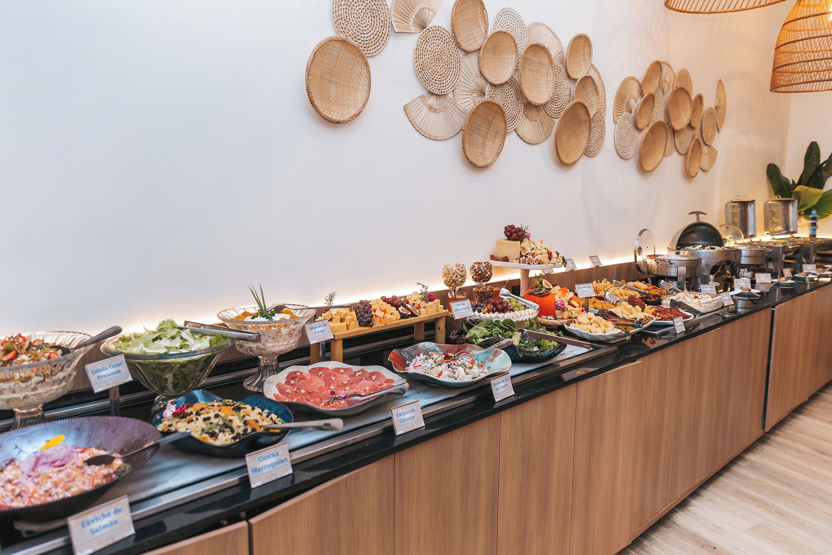 Un bufé con diversos alimentos y etiquetas, incluyendo ensaladas, carnes y quesos.
