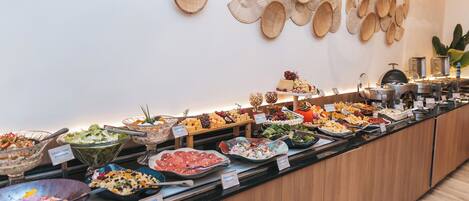 Un bufé con diversos alimentos y etiquetas, incluyendo ensaladas, carnes y quesos.