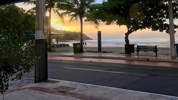 A coastal walkway with benches, palm trees, and a view of the ocean at sunset.