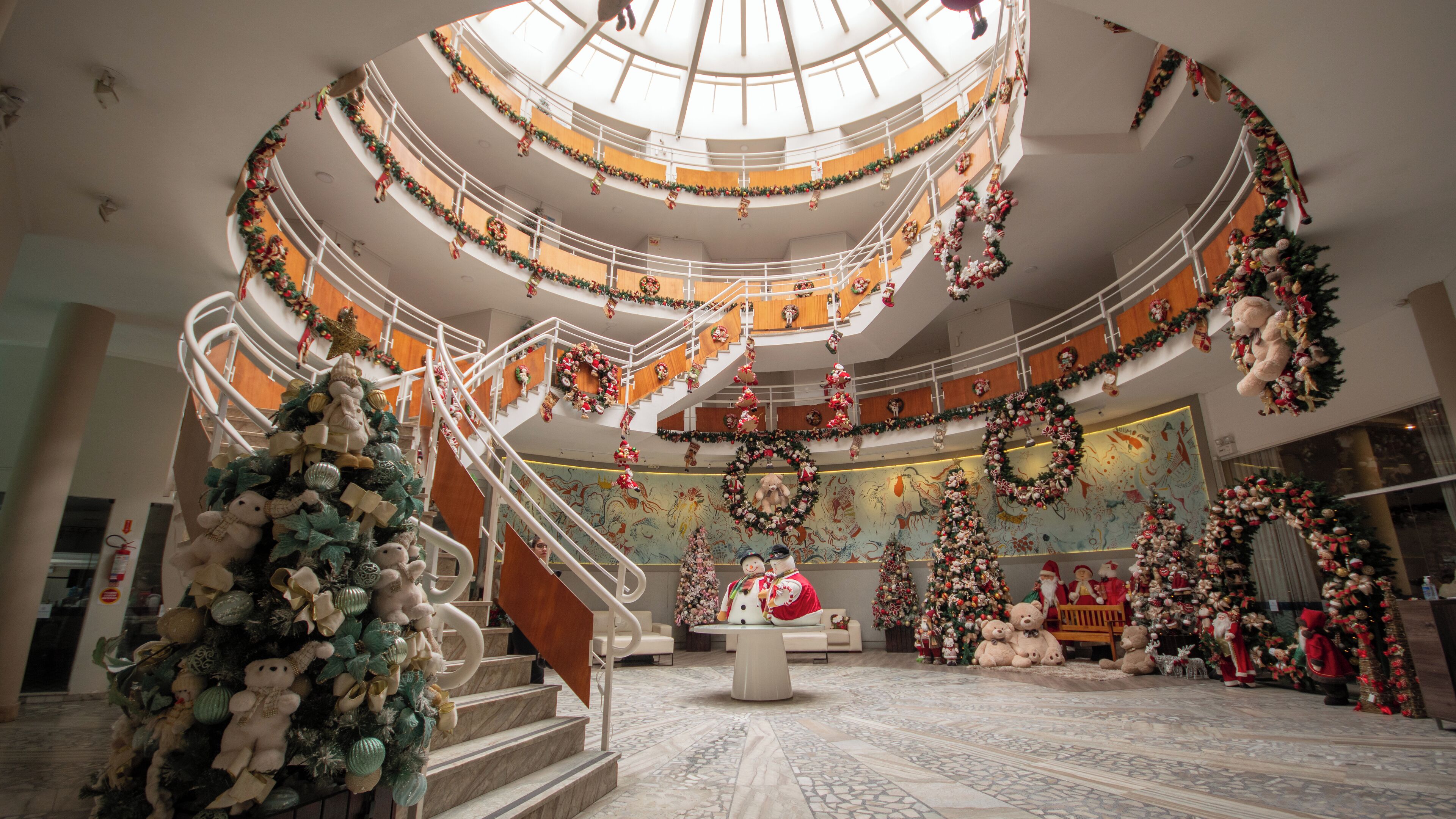 A multi-level atrium decorated with Christmas ornaments, a central staircase, and a large Christmas tree.