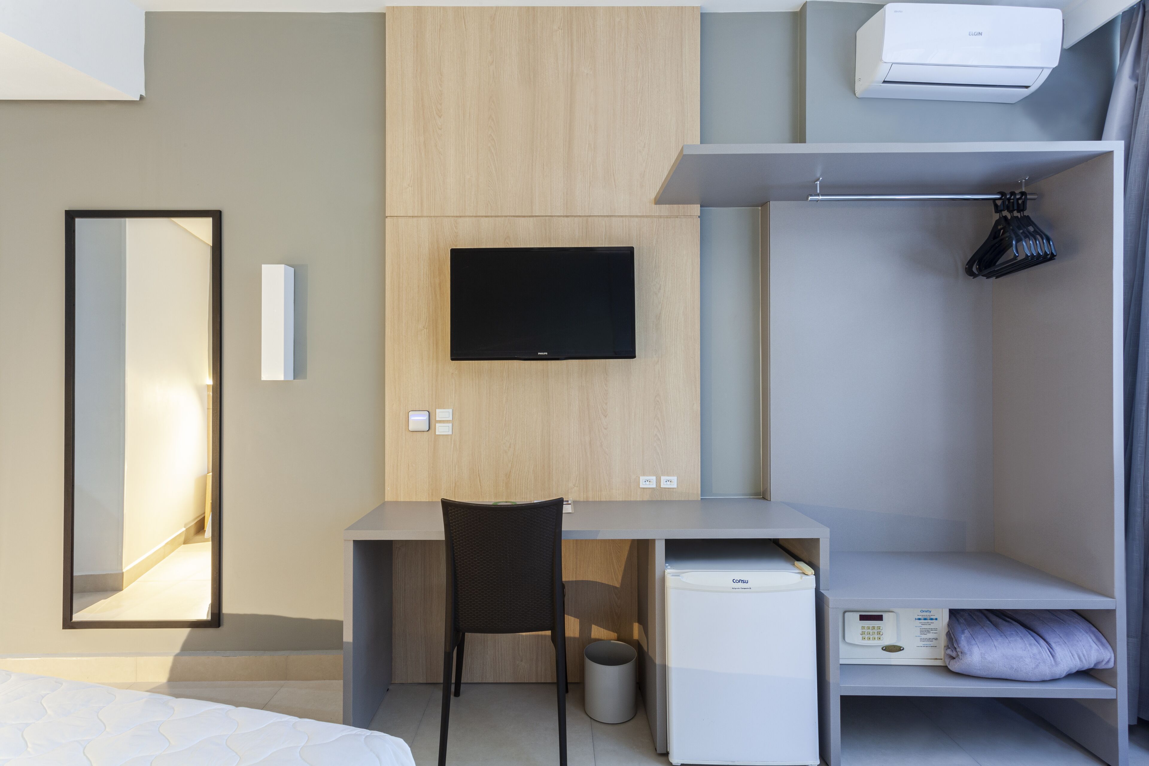 Una habitación de hotel moderna con una cama, un escritorio con silla, televisor, minibar y armario.