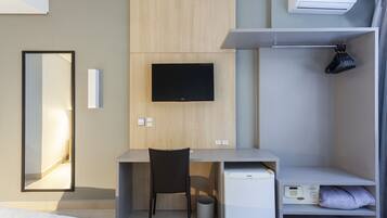 Una habitación de hotel moderna con una cama, un escritorio con silla, televisor, minibar y armario.