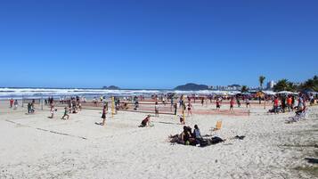 Una cancha de voleibol de playa con gente jugando, rodeada de arena y vistas al océano.