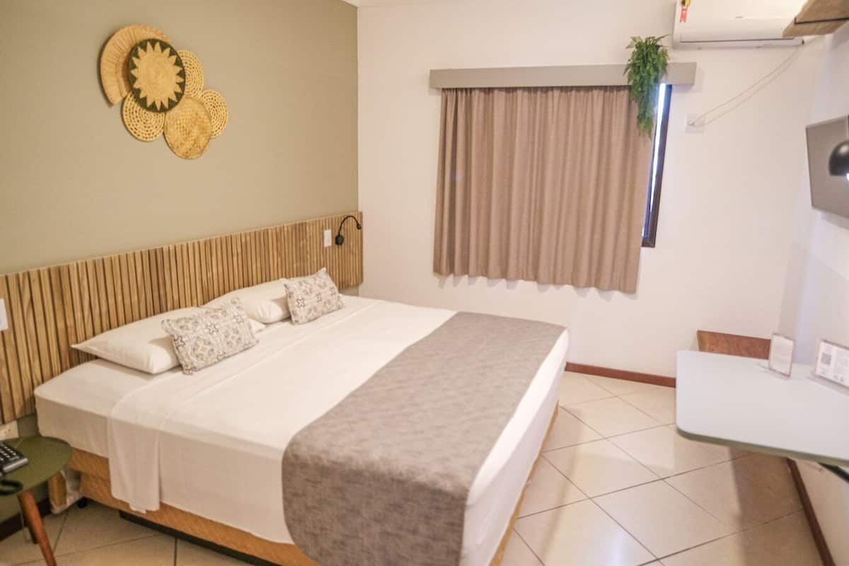 Quarto bem arrumado com cama, mesa de cabeceira e pequena escrivaninha.