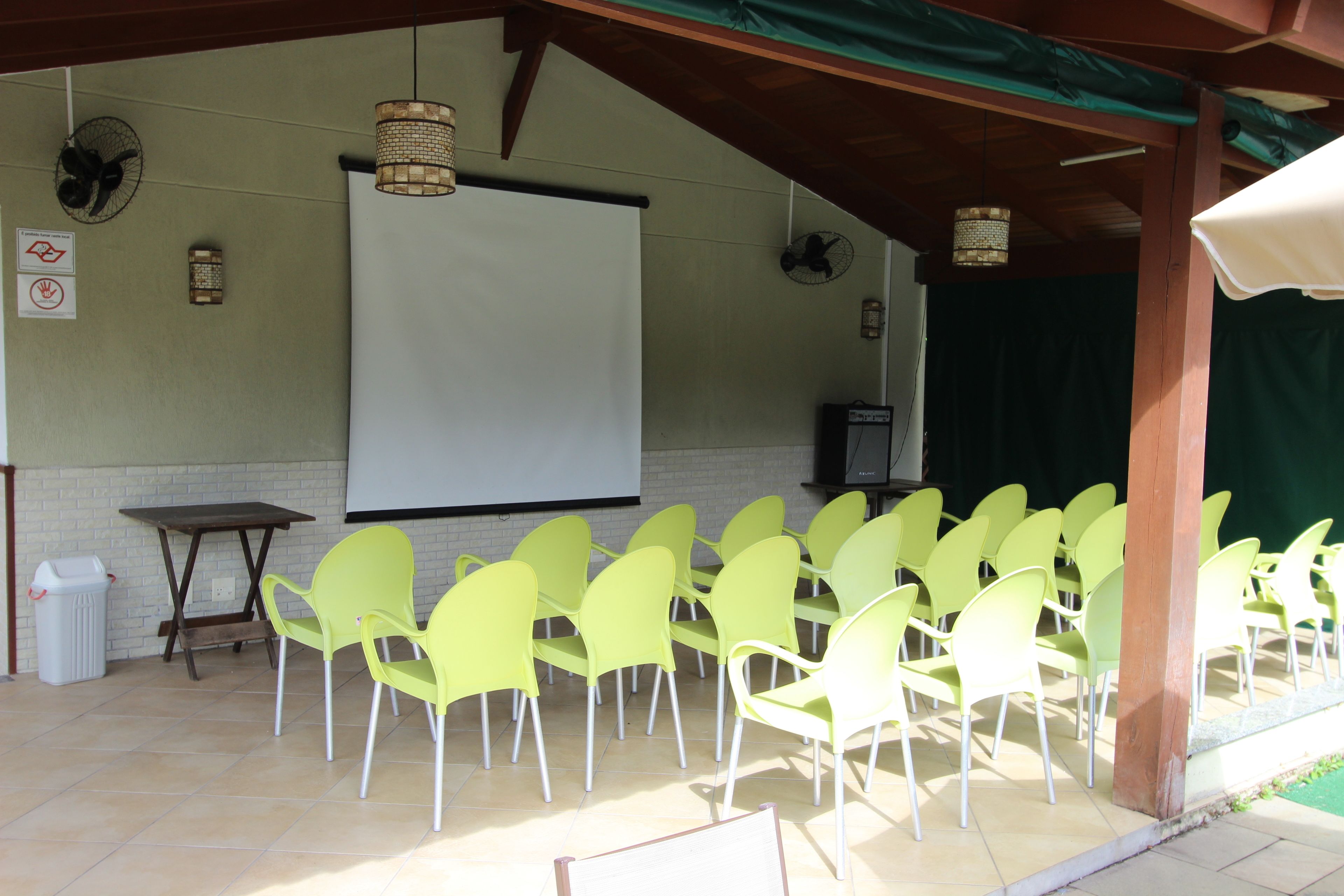 A covered outdoor seating area with a white projection screen, multiple chairs, and a table.