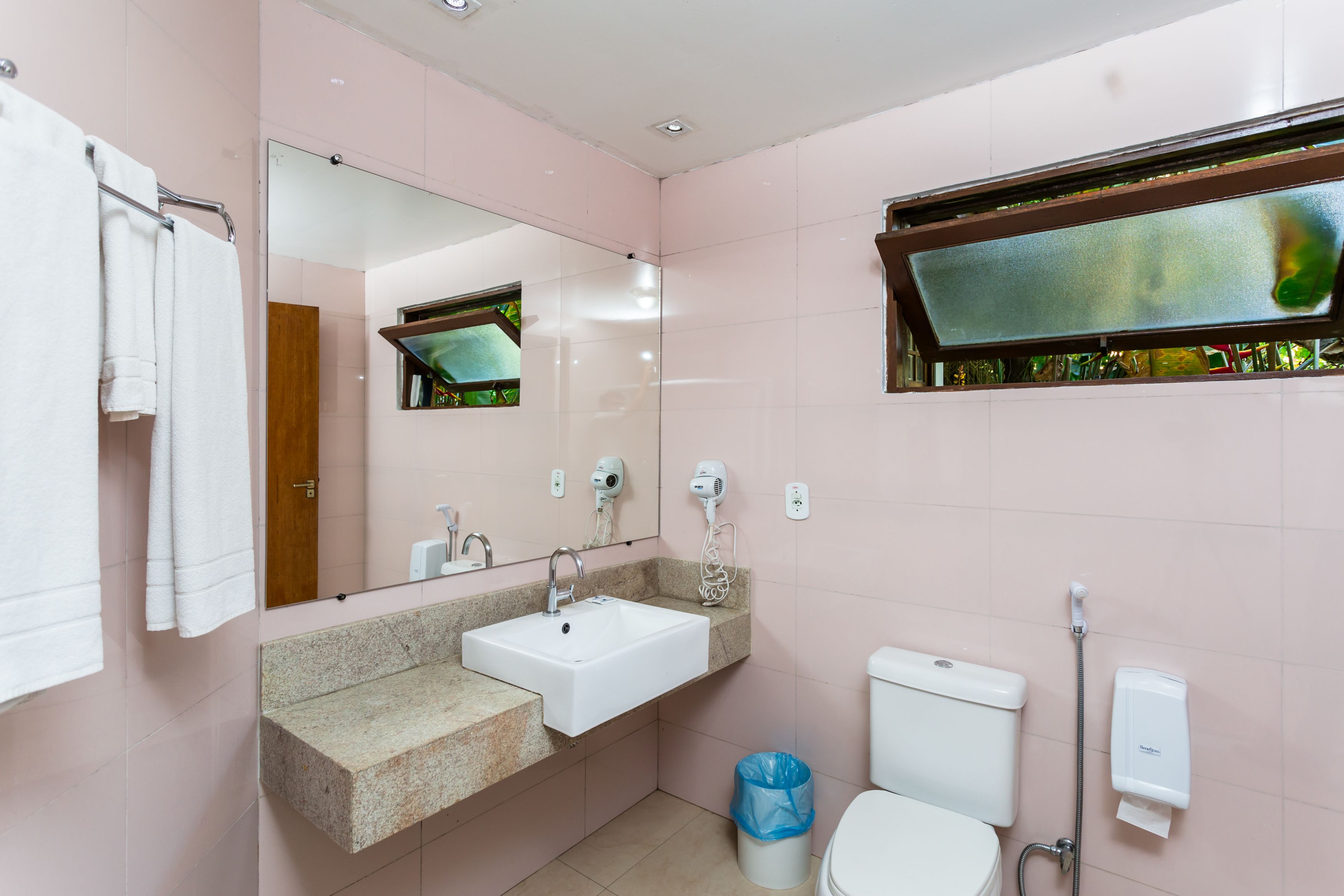 A bathroom with a sink, mirror, towel rack, toilet, and a window with a view.