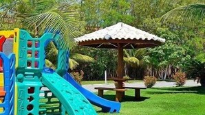 A playground with a slide and climbing structures, surrounded by palm trees and grass. - Atlantida Park Hotel (Porto Seguro)