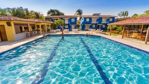 A clear blue swimming pool with a diving board, surrounded by buildings with tiled roofs and outdoor seating areas.