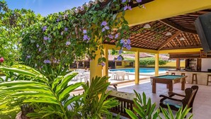 A covered outdoor area with a pool, lounge chairs, and a billiards table.